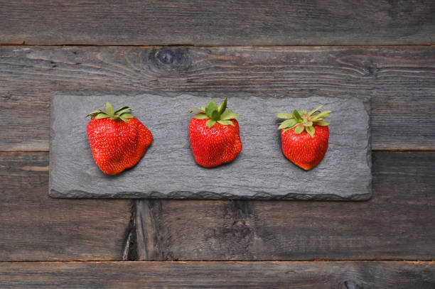 three strawberries on a dark wooden background