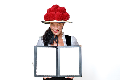 Black Forest waitress in a traditional Bollenhut with red pompoms who winks mischievously and holding open a blank menu with copy space with a friendly smile