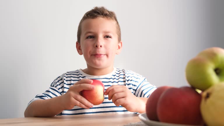 A handsome boy eats a big ripe red apple for breakfast. Healthy food with fruits