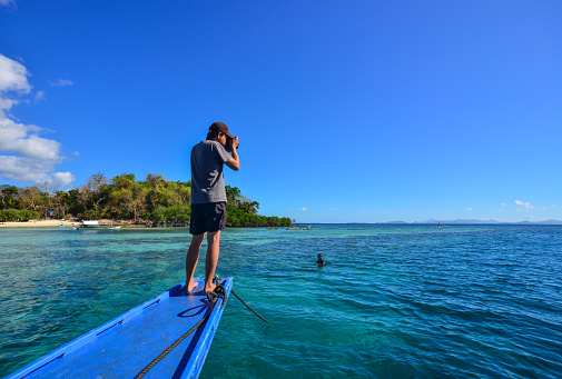 Coron, Philippines - Apr 9, 2017. An Asian man standing on wooden boat and taking pictures the blue sea.