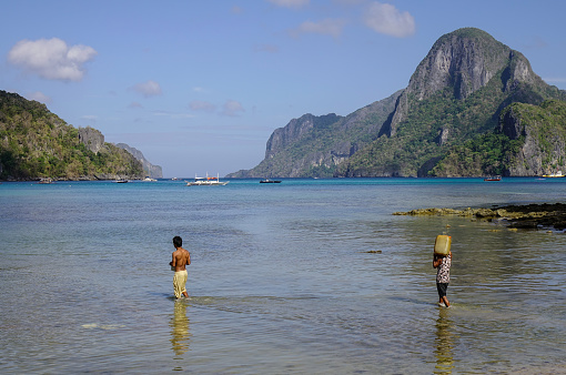 El Nido, Philippines - Apr 7, 2017. People walking on the beach with green island background at sunny day.