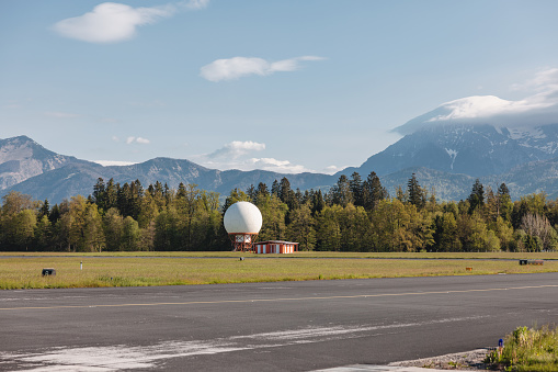 An empty airport runway, asphalt road with wind indicators, mountains in the background.