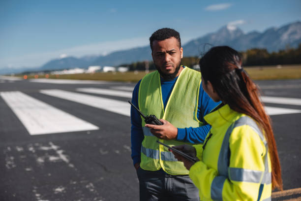 istock Multi Ethnic Airport Workers Wearing Yellow Safety Jackets While Standing In The Middle Off An Airstrip 1626764075