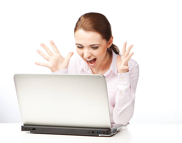 Young woman sitting at a laptop, screaming and gesticulating stock photo