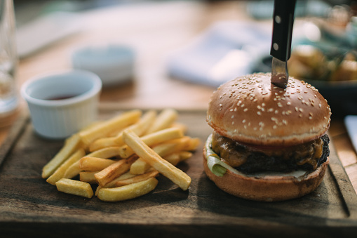 Close-up of beef burger in a sesame bun with french fries on the wooden plate, no people