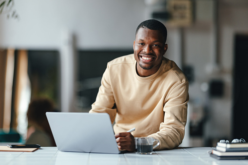 A portrait of a smiling African-American entrepreneur sitting at his laptop in the office.