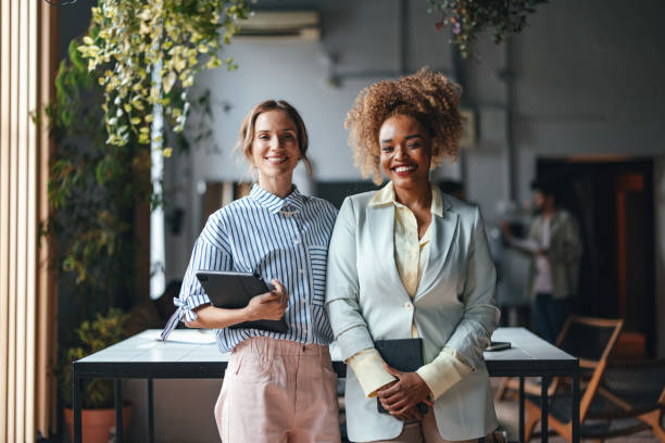 two happy beautiful blonde businesswomen looking at camera while standing in the office - två människor bildbanksfoton och bilder