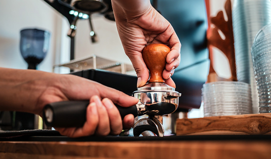 Close-up of hand Barista cafe making coffee with manual presses ground coffee using tamper at the coffee shop