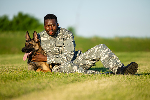 Portrait of soldier in military uniform in embrace with guard dog lying on the grass.