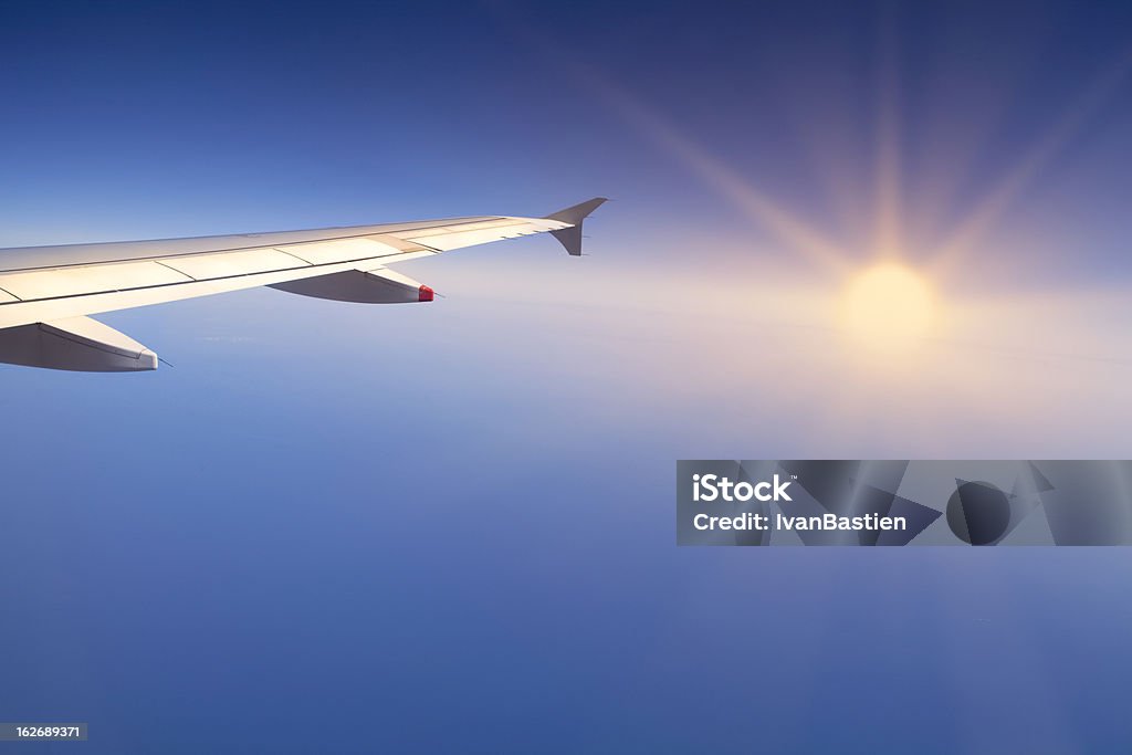 Flying over the sea at sunset The right wing of an airplane flying over Mediteranean sea. Setting sun in the background Aerial View Stock Photo