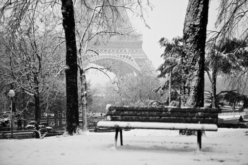 A bench in a public park near the Eiffel Tower in Paris, France on a snowy day.