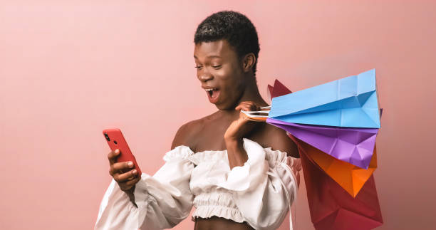 African transgender person using mobile phone while holding shopping bags. stock photo