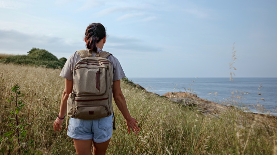 Join a spirited female traveler on an exhilarating hike through captivating landscapes in this mesmerizing photo. With a backpack filled with excitement and a heart full of wanderlust, she embarks on a vacation that celebrates the beauty of nature. As she treks through rugged terrain and embraces the freedom of the great outdoors, her joyful spirit shines through. With each step she takes, she immerses herself in the scenic beauty, basking in the warmth of the sunset. This adventurous woman epitomizes an active and carefree lifestyle, where every path becomes an exploration of self-discovery. Get inspired to embark on your own journey of wanderlust and let the harmony of nature and travel guide you to unforgettable experiences along the mesmerizing ocean's edge.