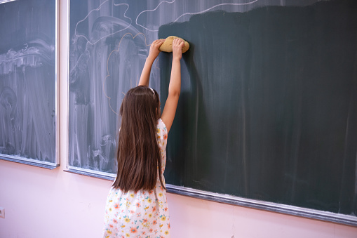 Little girl being told to clean the greenboard after the class has finished