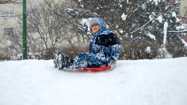 istock Cheerful smiling boy riding down the snowy hill on red plastic sleds during snowfall. 1626985637