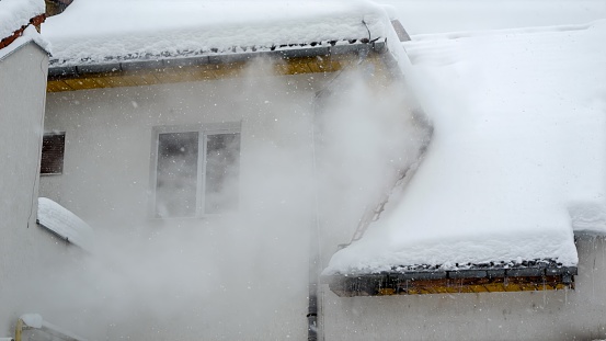 Smoke or water steam flowing from heating system of private house on snowy winter day. Concept of energy, ecology, heating and pollution.
