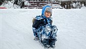 Joy of a child as he sleds down a snowy hill on his feet, with the footage slowed down to accentuate every moment of the thrilling ride.