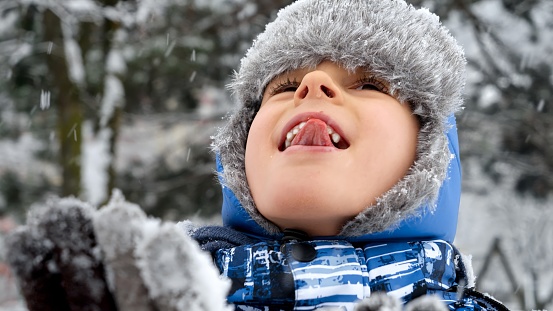 Young boy sticking out his tongue to catch snowflakes on a snowy day. Concept of playful winter activities