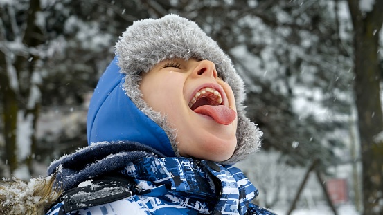 Portrait of boy joyfully catching snowflakes with his tongue during a winter snowfall. Concept of winter wonderland and outdoor fun