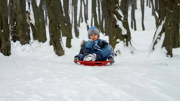 istock Happy and smiling young boy gleefully sliding down a snowy hill on his plastic sled. Essence of winter holidays and the fun and excitement of playing outdoors in the snow. 1626986871
