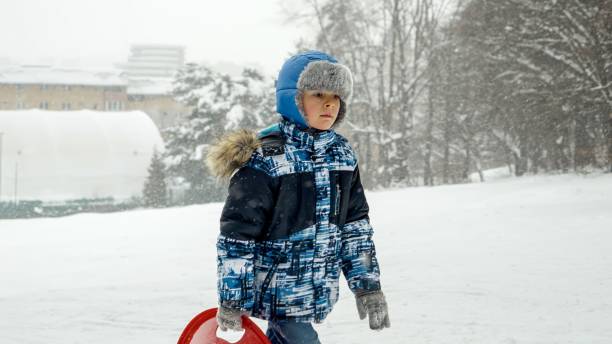 istock A smiling boy carries his sleds up a snow-covered hill, ready for an exciting ride down. Joy and wonder of winter playtime. 1626987353