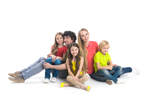 Portrait of happy family with three children sitting on the floor at studio isolated on white background
