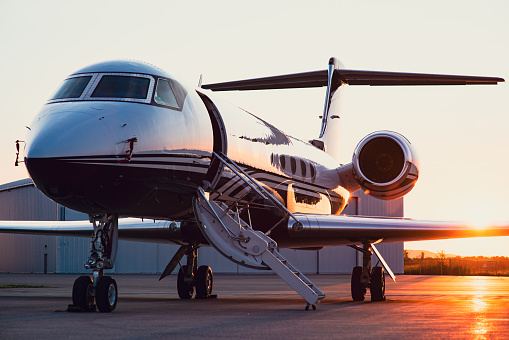 Private jet parked on the apron at a regional airport.  Setting sun in the background. Boarding stairs are extended.