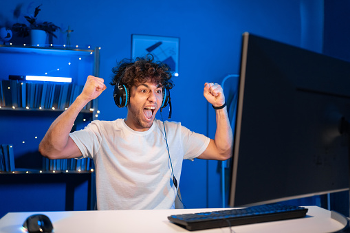 Arabic young male gamer winning in online video game on computer. Portrait of guy in headphones victory playing PvP tournament. Copy space