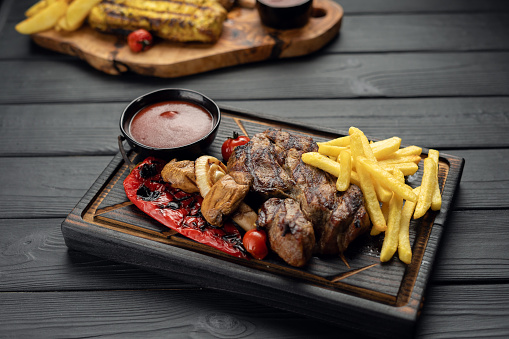 Striploin beef steak with french fries served on board on dark wooden background. Freshly meat grilled. Healthy dinner. Mediterranean Diet. Top view. Copy space