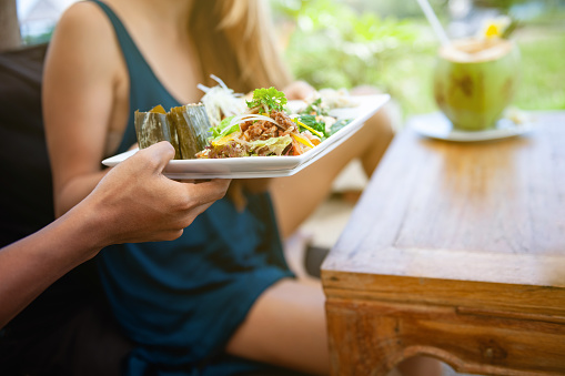 The waiter brings the customer a plate with food, the customer sits on the terrace at the table