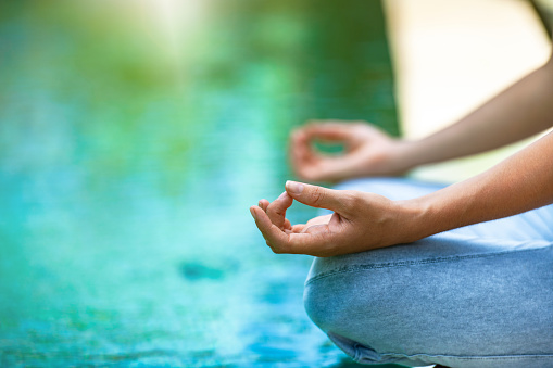 Young woman sits in the lotus position on the edge of a pool and meditates, copy space
