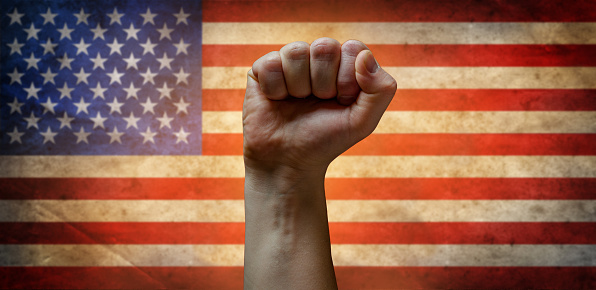 A man's fist against the background of the US flag as a symbol of protest, strike, demonstrations, struggle for rights, strength, victory, independence, fighting for a just cause and patriotism.