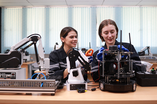 Caucasian two young female engineers learning robotic arm in training class together, innovation and development smart 4.0 factory concept.