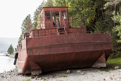 Rusty abandoned barge lays on the coast of Teletskoye lake. Altai Republic, Russia