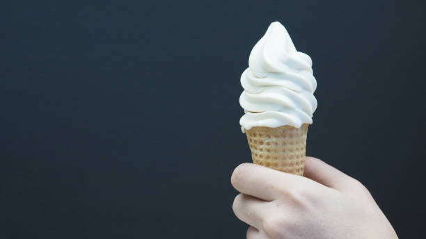 istock The hand is holding a soft-serve ice cream cone with a black background. 1627074097