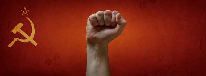 Fist of a protester against the background of the Soviet flag. Symbol of the struggle for rights. Soviet propaganda. Concept on the theme of the USSR, socialism, communism.