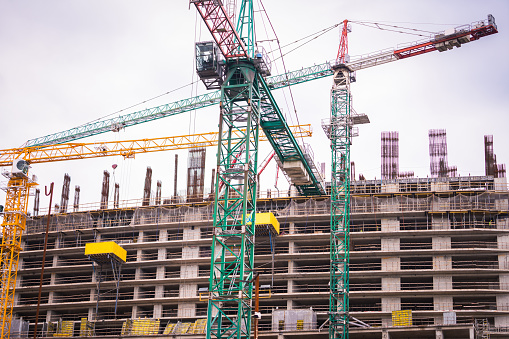 View of a multi-storey hotel under construction and many construction cranes against a cloudy sky,