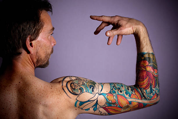 tattoo portrait mid adult man holding his arm aloft with fingers on hands tweaked and head and face in profile.  horizontal composition. forearm tattoos men stock pictures, royalty-free photos & images