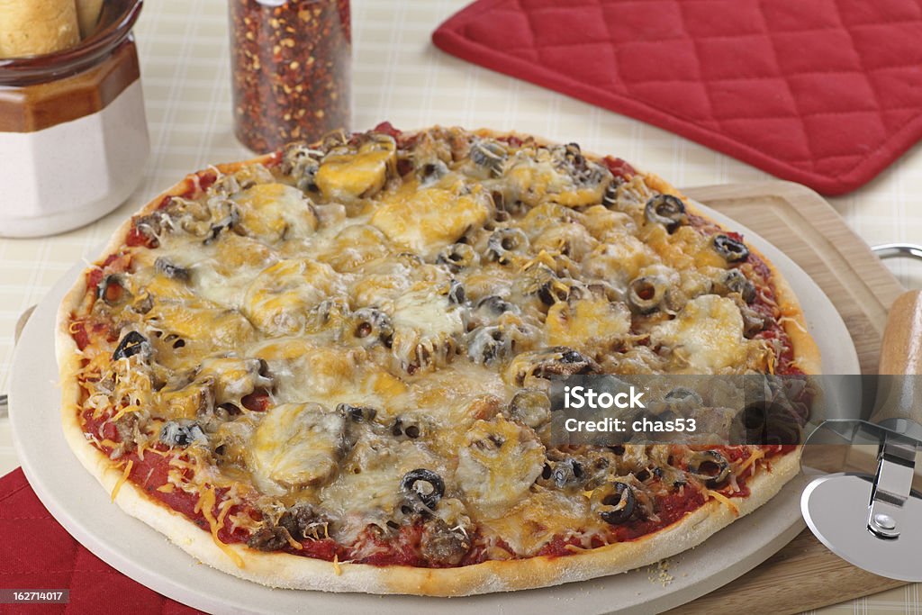 Sausage and Mushroom Pizza Whole sausage, mushroom and olive pizza on a baking stone Baked Stock Photo