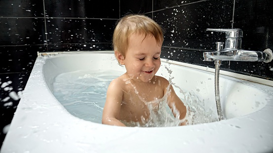 Little baby boy enjoying his bath time and playing with water, foam and sponge. The image highlights the significance of bath time as an essential part of a baby's hygiene routine.
