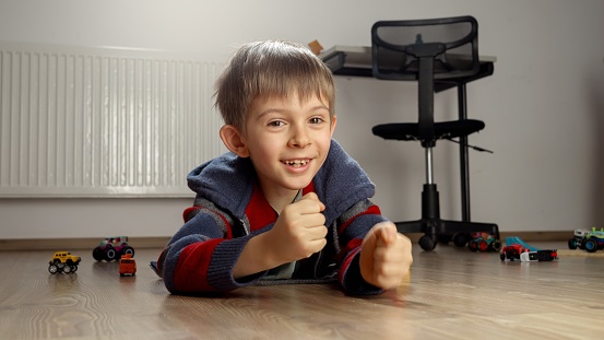 Cheerful smiling boy lying on floor and cheering after playing game.