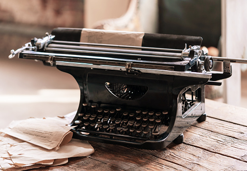 Vintage aged black typewriter with old paper blank on wooden table. Retro style photo.