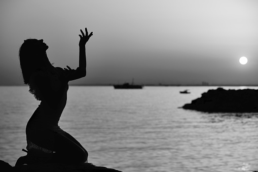 serene woman sitting at coast line and posing at sunset with different hand movements and signs