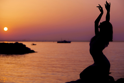 serene woman sitting at coast line and posing at sunset with different hand movements and signs