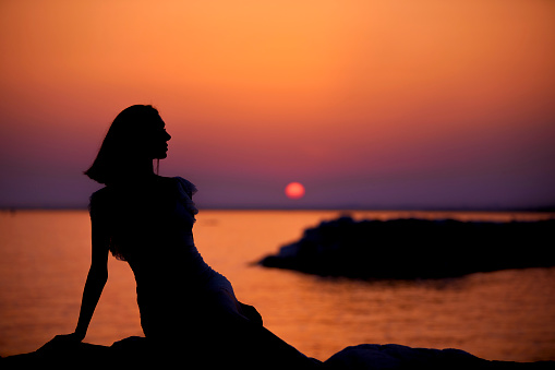 serene woman sitting at coast line and posing at sunset with different hand movements and signs