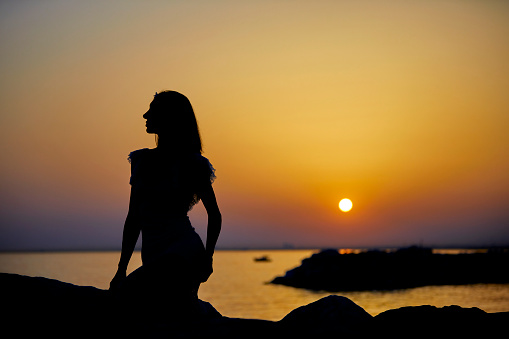 serene woman sitting at coast line and posing at sunset with different hand movements and signs