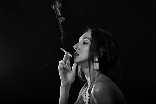 black and white photo of a young and attractive lady in studio smoking cigarette between smokes under dramatic light