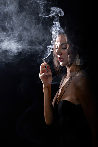 young and attractive lady in studio smoking cigarette between smokes under dramatic light