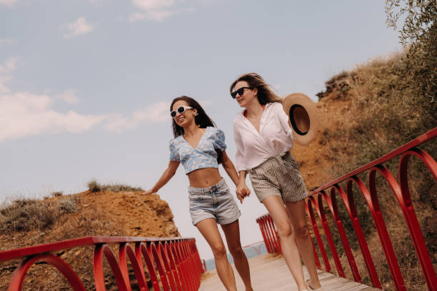istock Two joyful young women holding hands and smiling while running outdoors together 1627217084