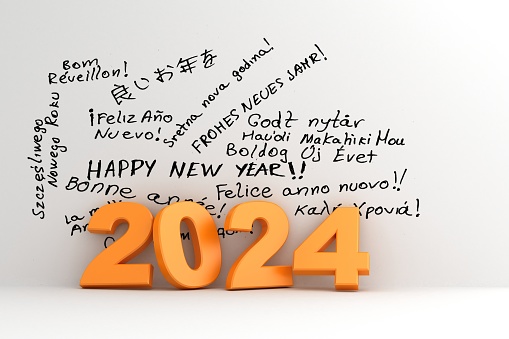 Year 2024. Orange numbers against a white wall with the greeting happy new year handwritten in many languages